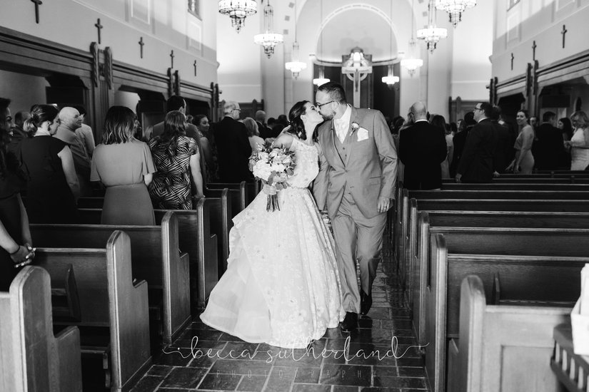 Bride and groom kiss while walking down aisle