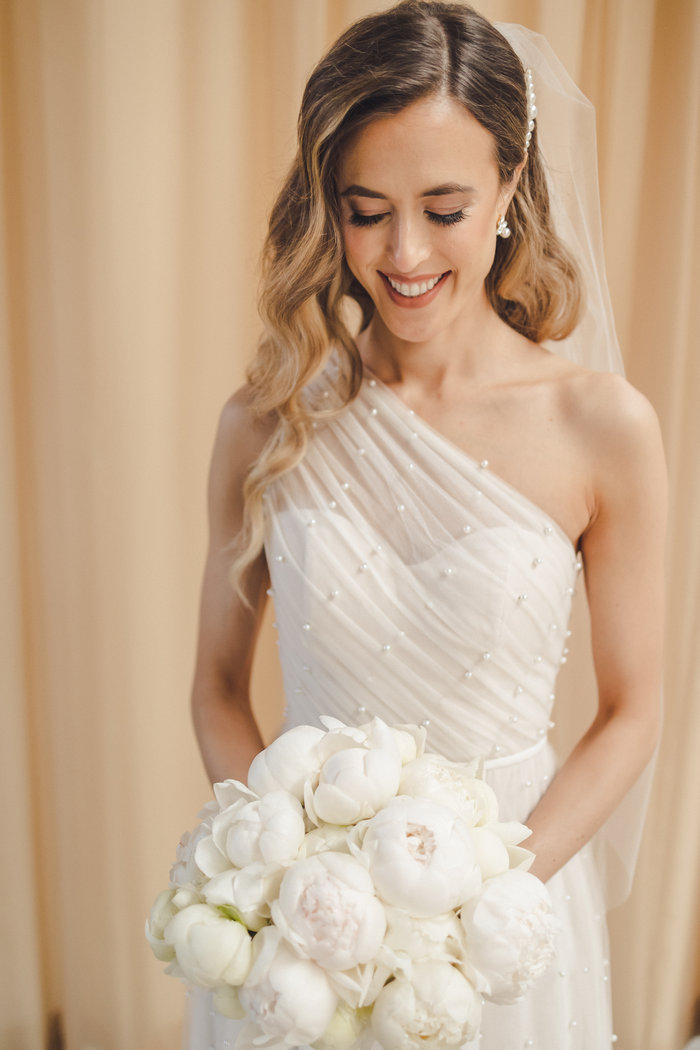 Bride portrait looking down; one shoulder gown with closed peony white bouquet